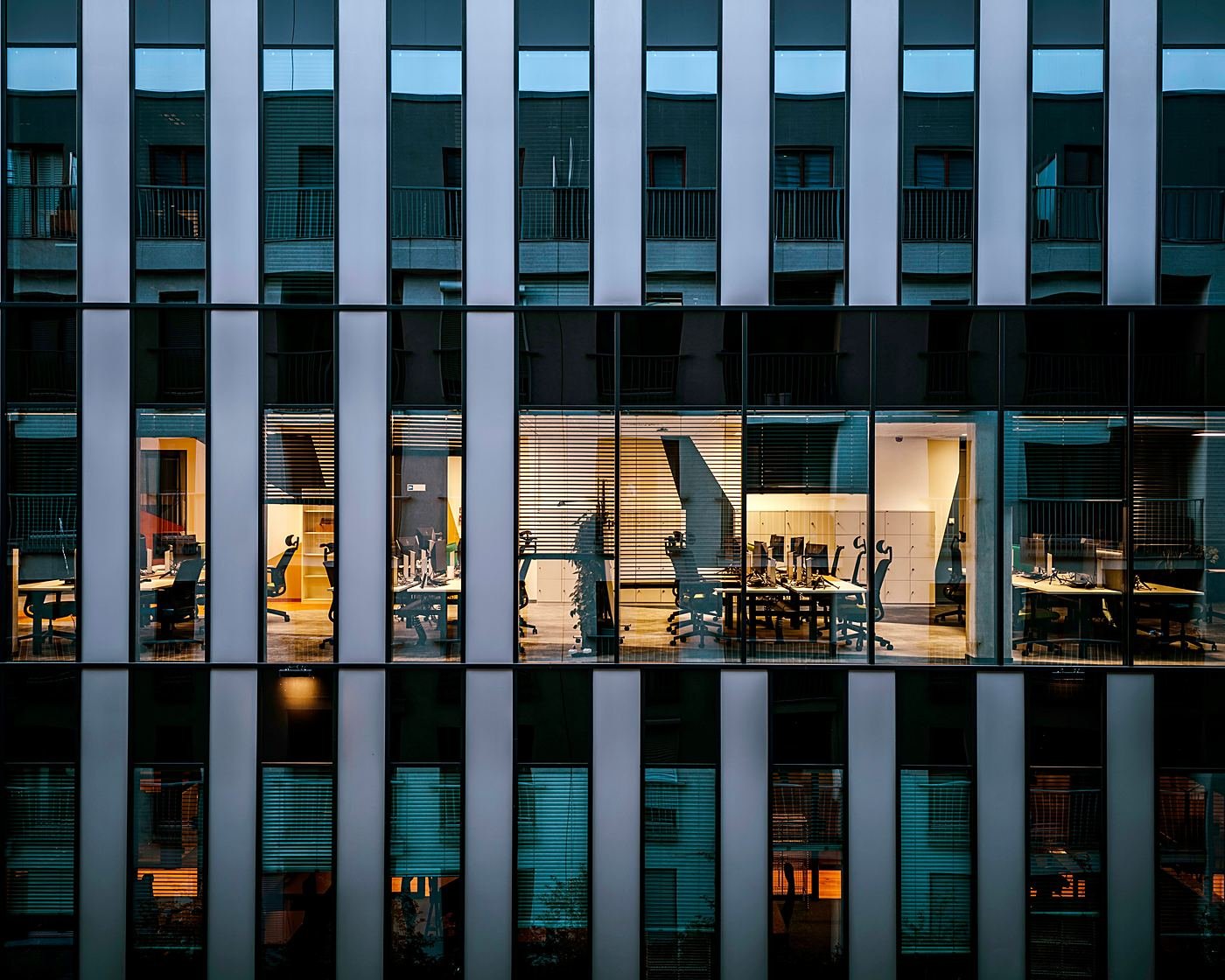 An office building at dusk, desks still lit behind the glass